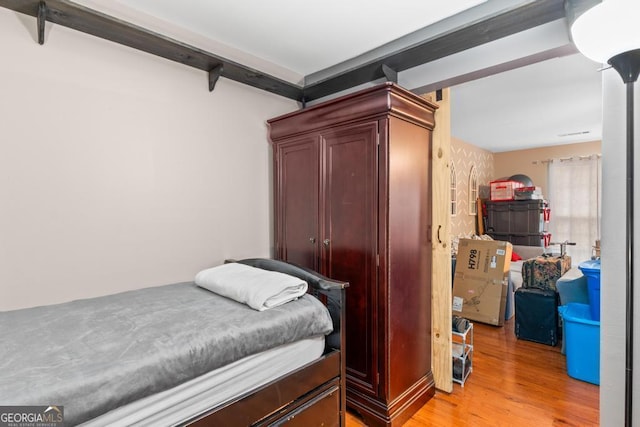 bedroom featuring beam ceiling and light wood-style floors