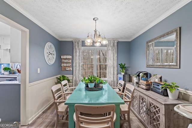 dining area featuring a textured ceiling, wood finished floors, wainscoting, crown molding, and a notable chandelier