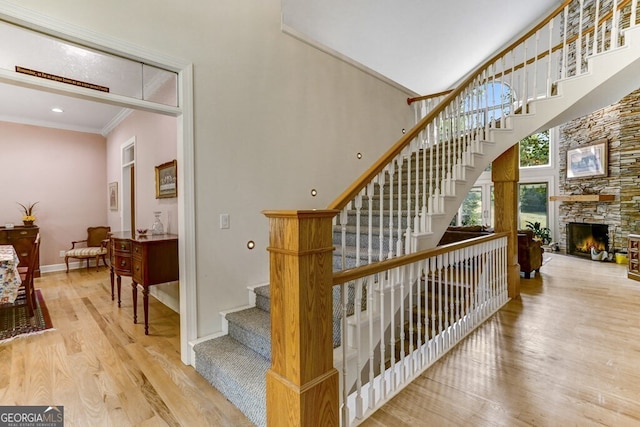 stairway with baseboards, ornamental molding, a fireplace, a high ceiling, and wood finished floors