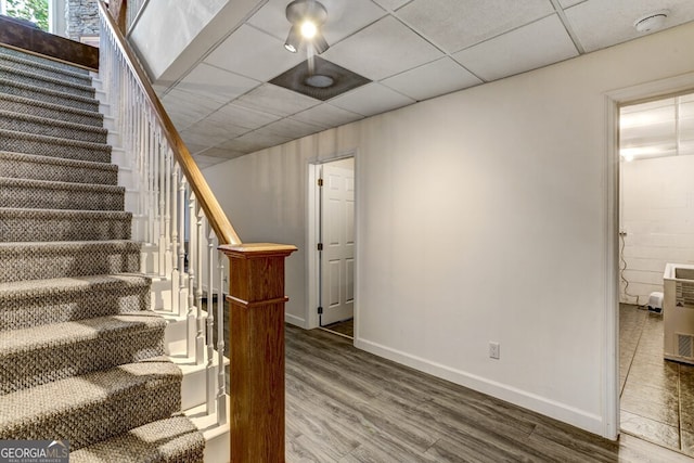 stairs featuring wood finished floors, baseboards, and a drop ceiling