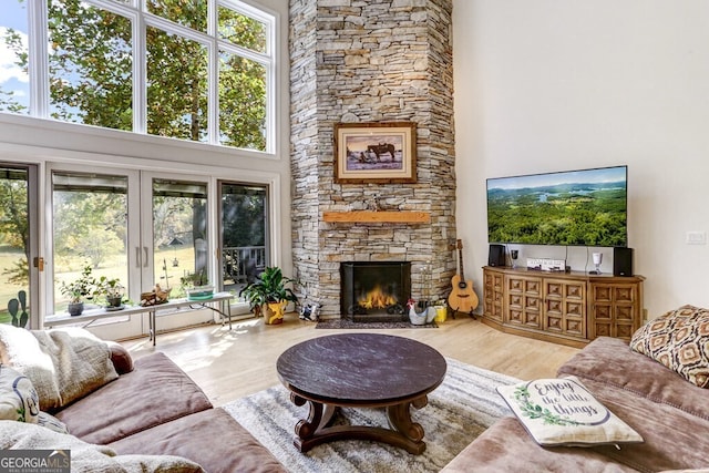 living room featuring a stone fireplace, a towering ceiling, and wood finished floors