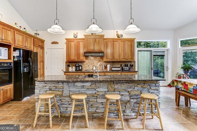 kitchen with under cabinet range hood, a breakfast bar, vaulted ceiling, decorative backsplash, and black appliances