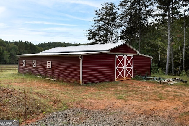 view of outbuilding with a wooded view, an outdoor structure, and fence