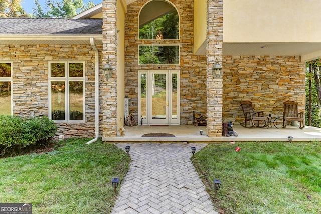 doorway to property featuring french doors, stone siding, and a lawn