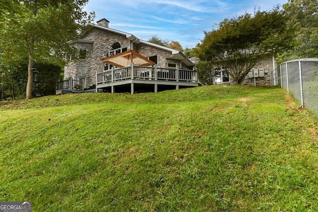 rear view of property featuring a deck, fence, a lawn, and stone siding