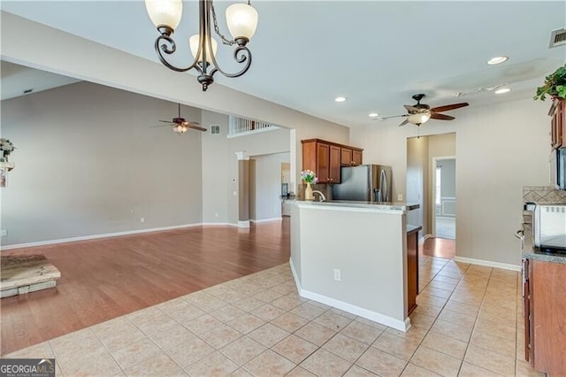 kitchen featuring stainless steel fridge, light tile patterned flooring, brown cabinetry, and ceiling fan with notable chandelier