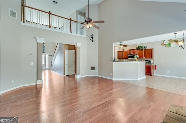 unfurnished living room featuring light wood-type flooring, visible vents, baseboards, and ceiling fan with notable chandelier