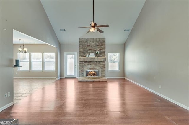 unfurnished living room featuring a stone fireplace, a healthy amount of sunlight, ceiling fan with notable chandelier, and visible vents