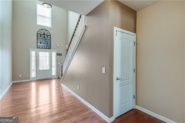 foyer entrance featuring wood finished floors, baseboards, and a towering ceiling