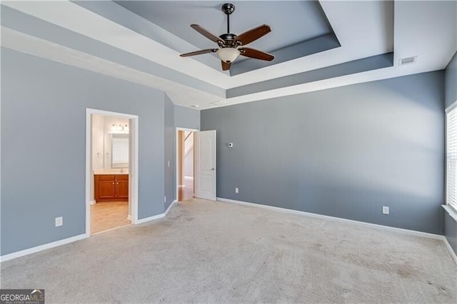 unfurnished bedroom with visible vents, ensuite bathroom, a tray ceiling, carpet, and baseboards