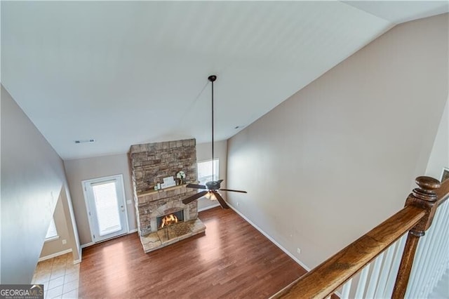 living area with baseboards, lofted ceiling, a fireplace, wood finished floors, and a ceiling fan