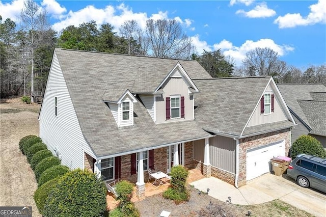 view of front of home featuring stone siding, a porch, roof with shingles, concrete driveway, and a garage