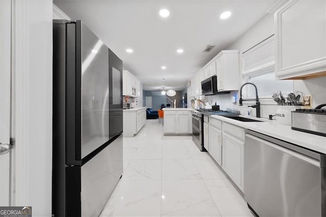 kitchen with a sink, light countertops, appliances with stainless steel finishes, white cabinetry, and marble finish floor