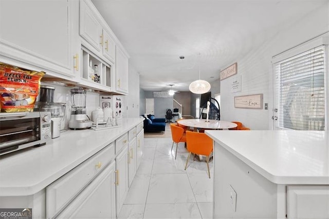 kitchen with a toaster, light countertops, pendant lighting, white cabinetry, and marble finish floor