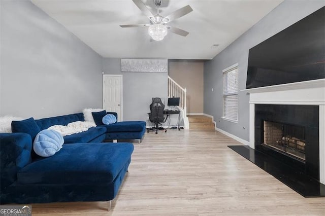 living area with wood finished floors, baseboards, a ceiling fan, a fireplace with raised hearth, and stairs