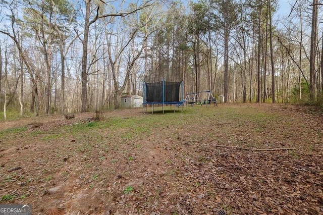 view of yard with a trampoline, an outdoor structure, and a shed