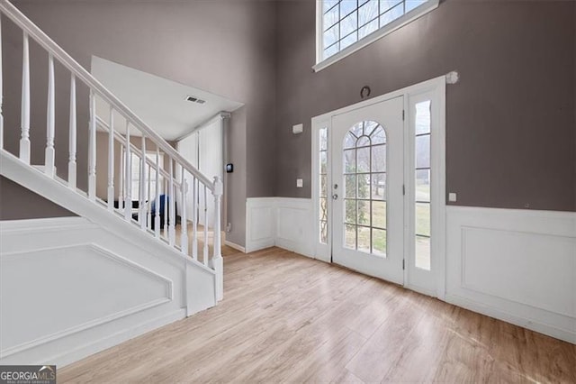 foyer entrance with visible vents, stairs, wainscoting, wood finished floors, and a decorative wall