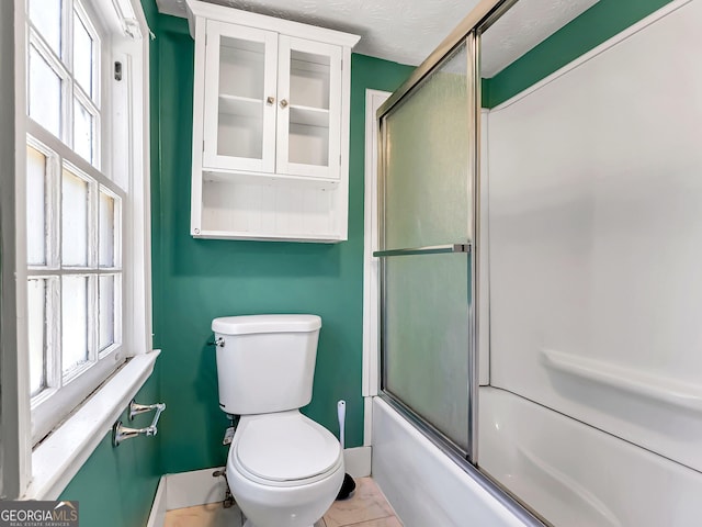 full bath featuring plenty of natural light, a textured ceiling, toilet, and shower / bath combination with glass door