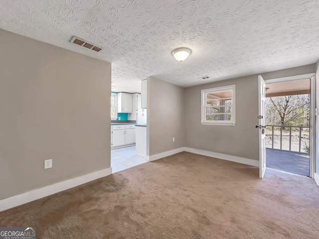 unfurnished room featuring visible vents, light colored carpet, a textured ceiling, and baseboards