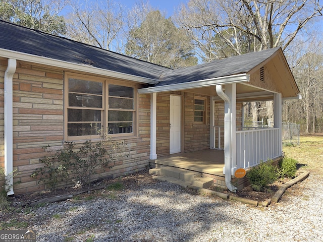 exterior space with covered porch, stone siding, and a shingled roof