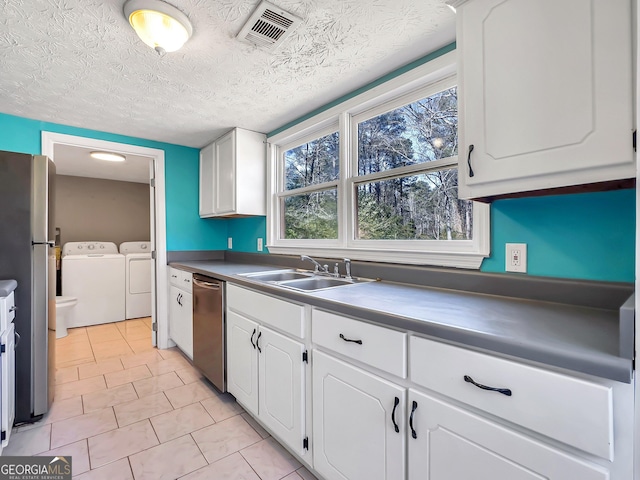 kitchen featuring visible vents, washer and dryer, a sink, stainless steel appliances, and white cabinets