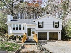 raised ranch with a garage, a chimney, and aphalt driveway