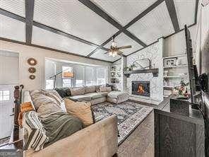 living room with a stone fireplace, beamed ceiling, and ceiling fan