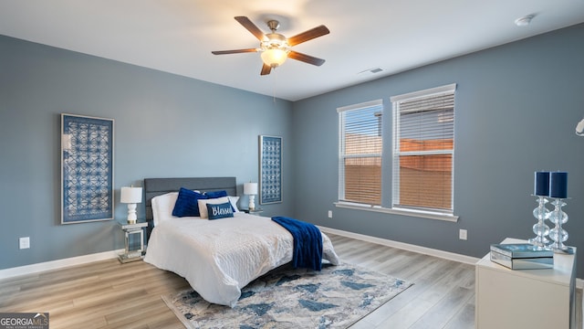 bedroom with a ceiling fan, wood finished floors, visible vents, and baseboards