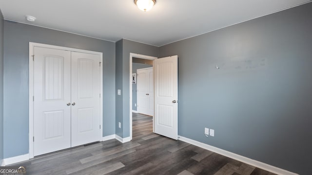 unfurnished bedroom with dark wood-style floors, baseboards, and a closet