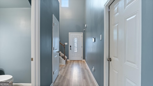 entrance foyer featuring stairway, baseboards, light wood-style floors, and a towering ceiling