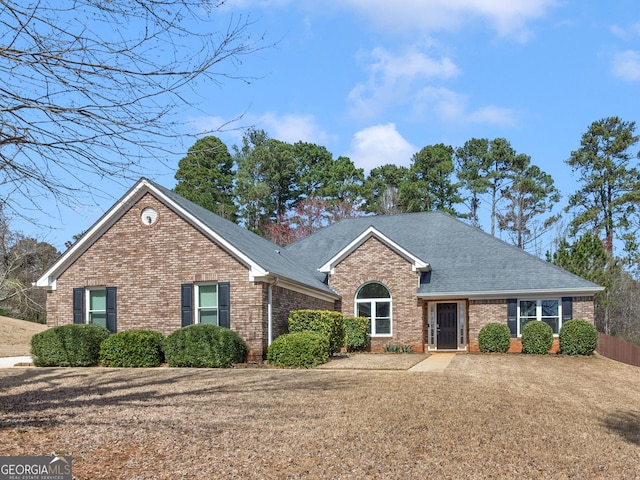 ranch-style home featuring brick siding, roof with shingles, and fence