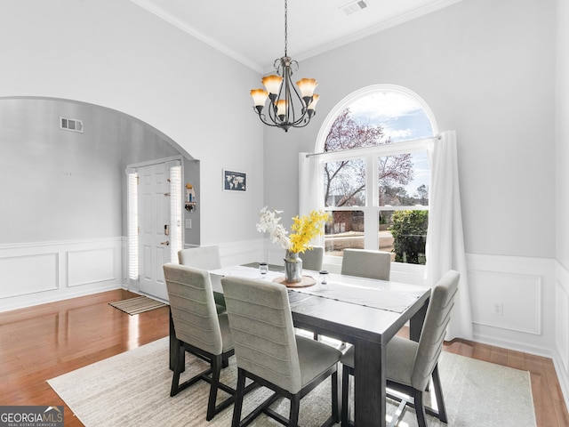 dining room with wood finished floors, visible vents, an inviting chandelier, arched walkways, and wainscoting