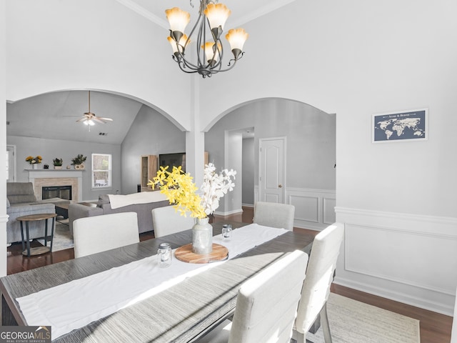 dining area featuring wood finished floors, a wainscoted wall, a glass covered fireplace, a decorative wall, and ceiling fan with notable chandelier