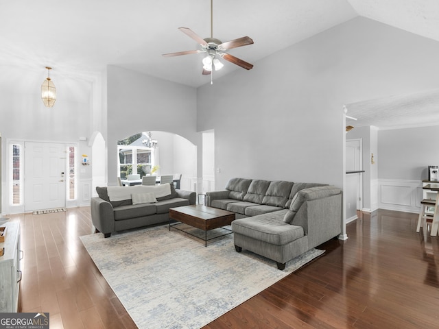 living area featuring dark wood finished floors, a decorative wall, arched walkways, and wainscoting