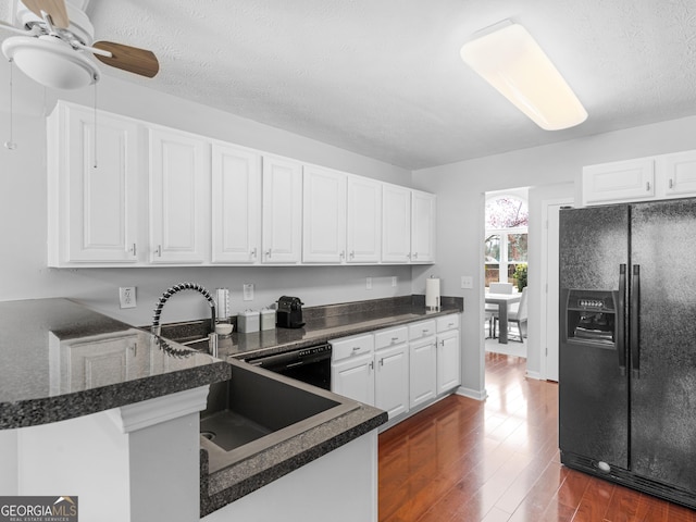 kitchen featuring black fridge, a sink, dark wood-style floors, a peninsula, and white cabinets