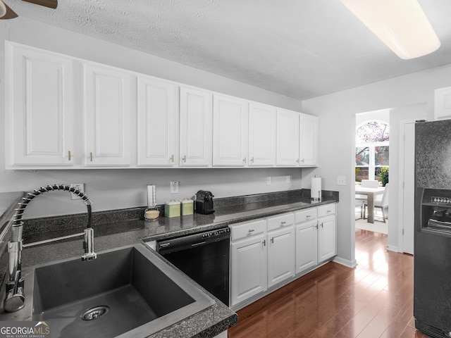 kitchen with a sink, black appliances, dark wood-style flooring, and white cabinetry