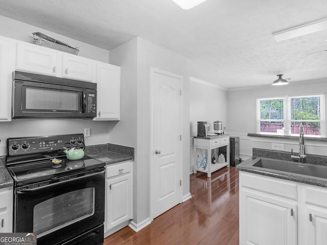 kitchen with black appliances, dark wood finished floors, a textured ceiling, white cabinetry, and a sink