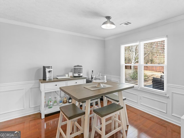 dining space with visible vents, a wainscoted wall, a textured ceiling, and wood finished floors