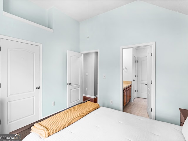 bedroom with light tile patterned floors, high vaulted ceiling, ensuite bathroom, and baseboards