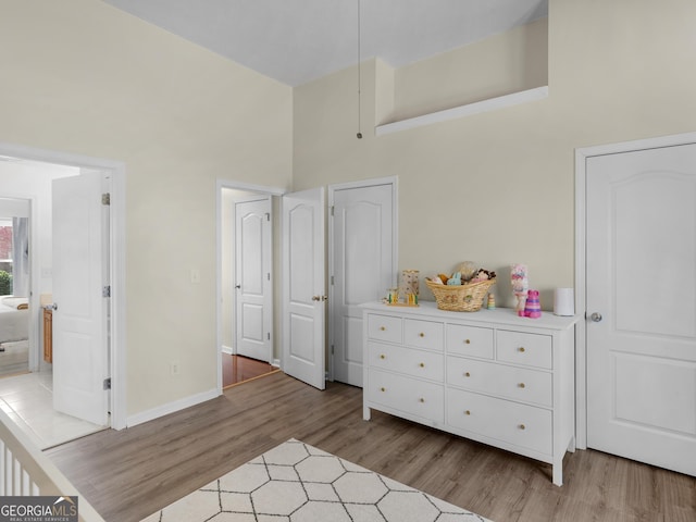 bedroom with baseboards, a high ceiling, and light wood-style floors