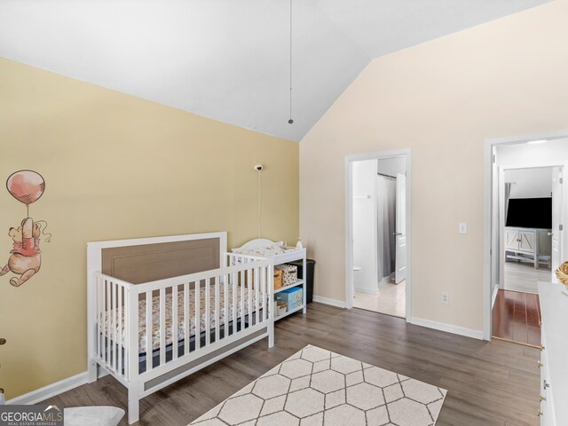 bedroom featuring a crib, wood finished floors, baseboards, and high vaulted ceiling