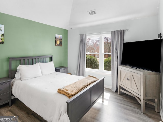 bedroom with lofted ceiling, wood finished floors, and visible vents