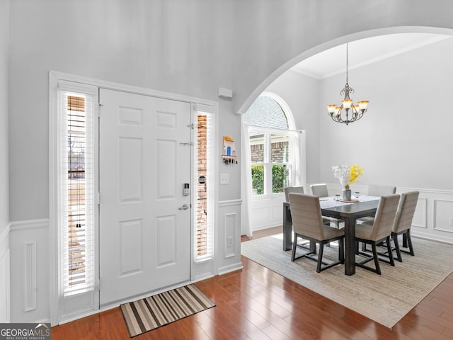 entryway with crown molding, dark wood-type flooring, a chandelier, a wainscoted wall, and a decorative wall