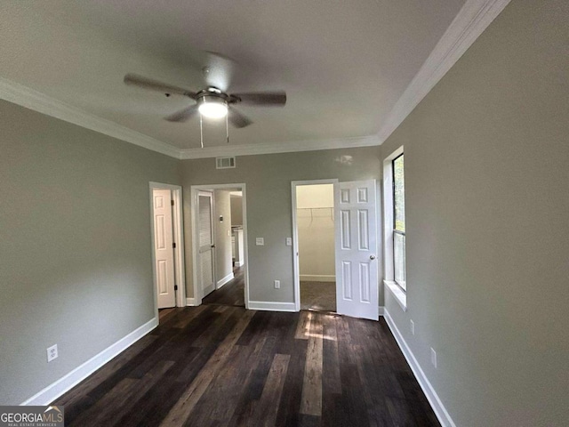 unfurnished bedroom featuring visible vents, dark wood-type flooring, crown molding, baseboards, and a spacious closet