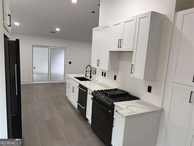 kitchen with light stone counters, wood finished floors, visible vents, a sink, and black appliances