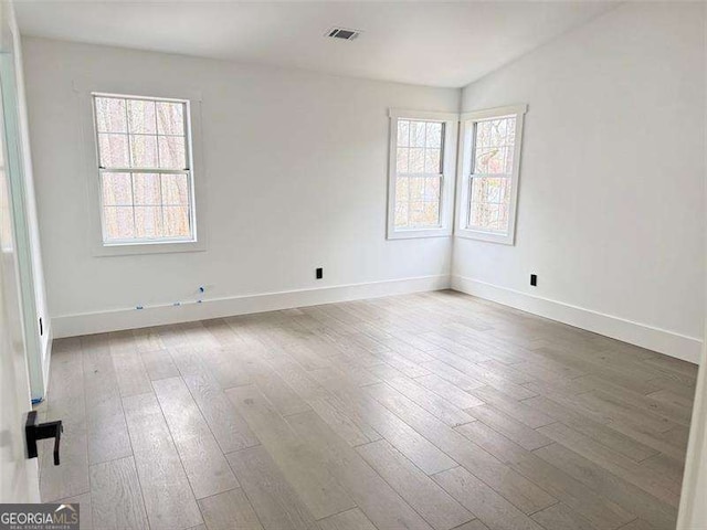 empty room with a wealth of natural light, visible vents, and wood finished floors