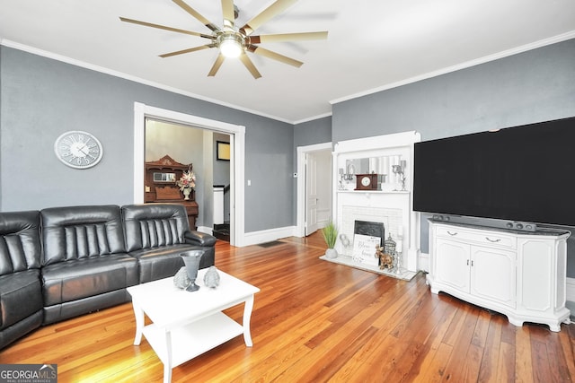 living room with a ceiling fan, baseboards, light wood finished floors, ornamental molding, and a brick fireplace