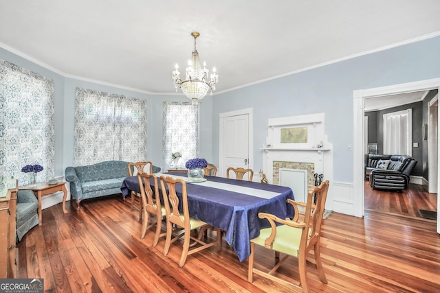 dining space featuring a fireplace, an inviting chandelier, hardwood / wood-style flooring, and crown molding