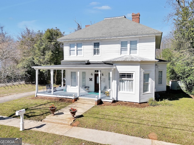 view of front of home with a front yard, covered porch, roof with shingles, and a chimney