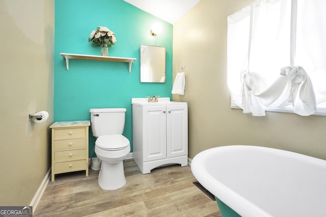 bathroom with toilet, wood finished floors, baseboards, a freestanding bath, and vanity